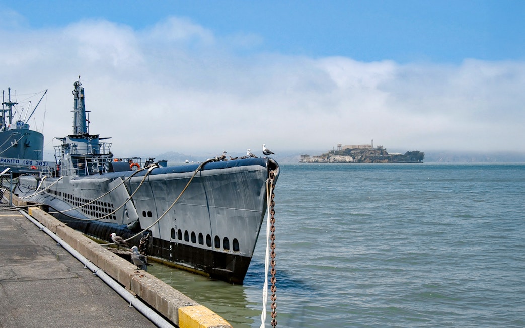 Submarine docked at San Francisco pier with Alcatraz Island in the background.