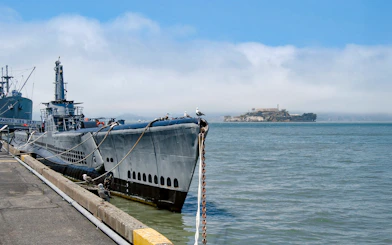 Submarine docked at San Francisco pier with Alcatraz Island in the background.