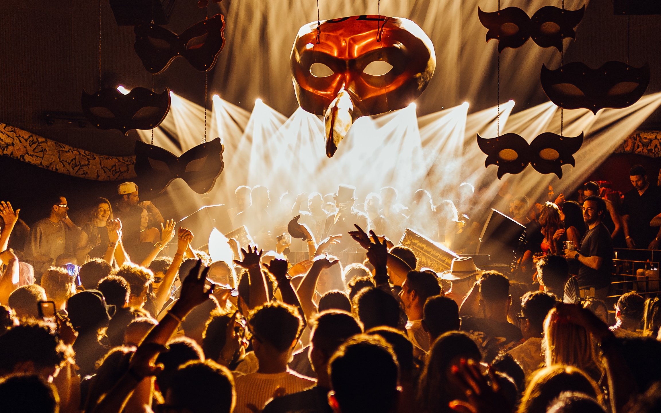 DJ performing at Club Chinois with crowd and masks, Ibiza.