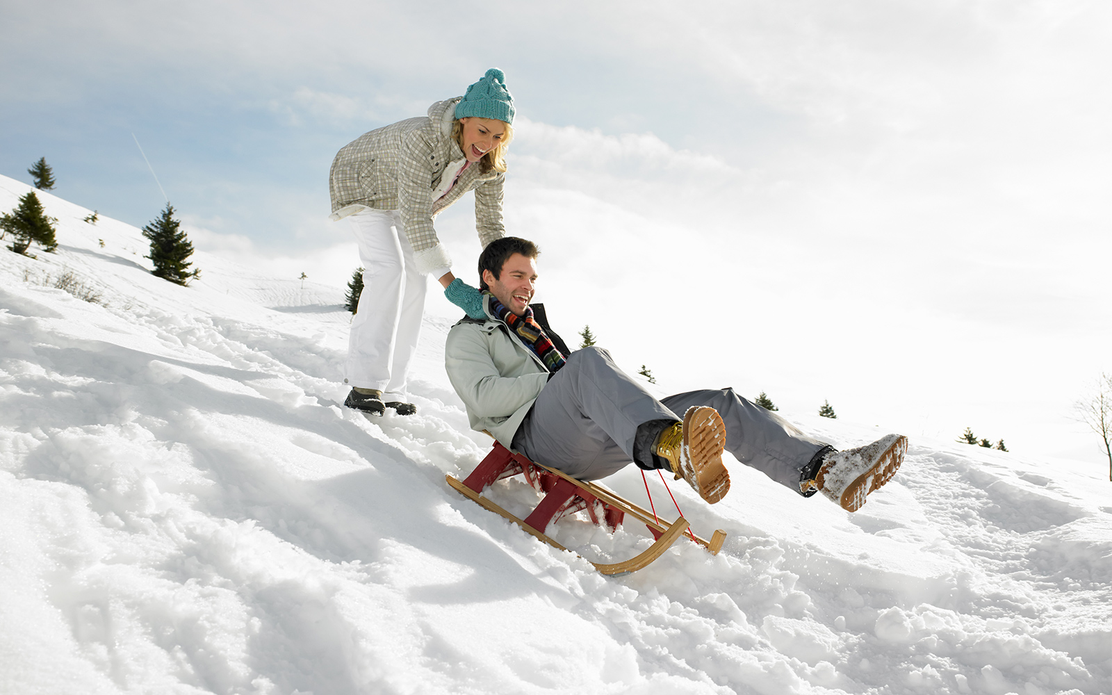 Sledding down a snowy hill with trees in the background.
