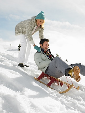 Sledding down a snowy hill with trees in the background.