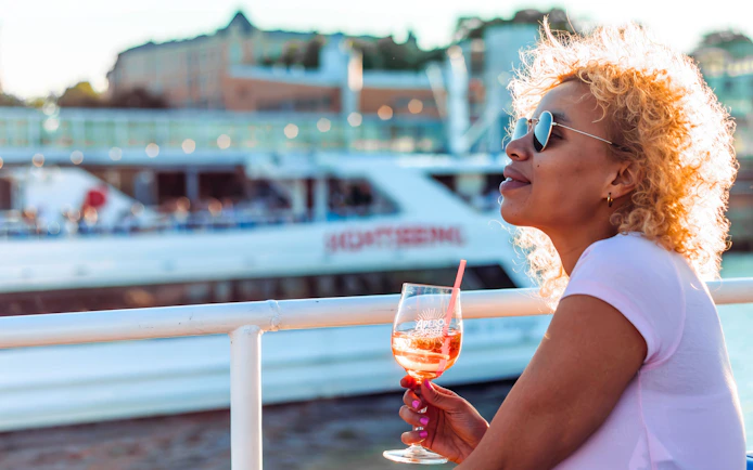 Guest enjoying a drink on the Helsinki sightseeing cruise with cityscape in background.