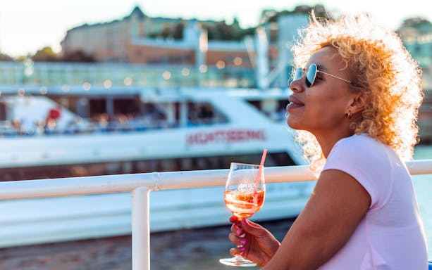 Guest enjoying a drink on the Helsinki sightseeing cruise with cityscape in background.