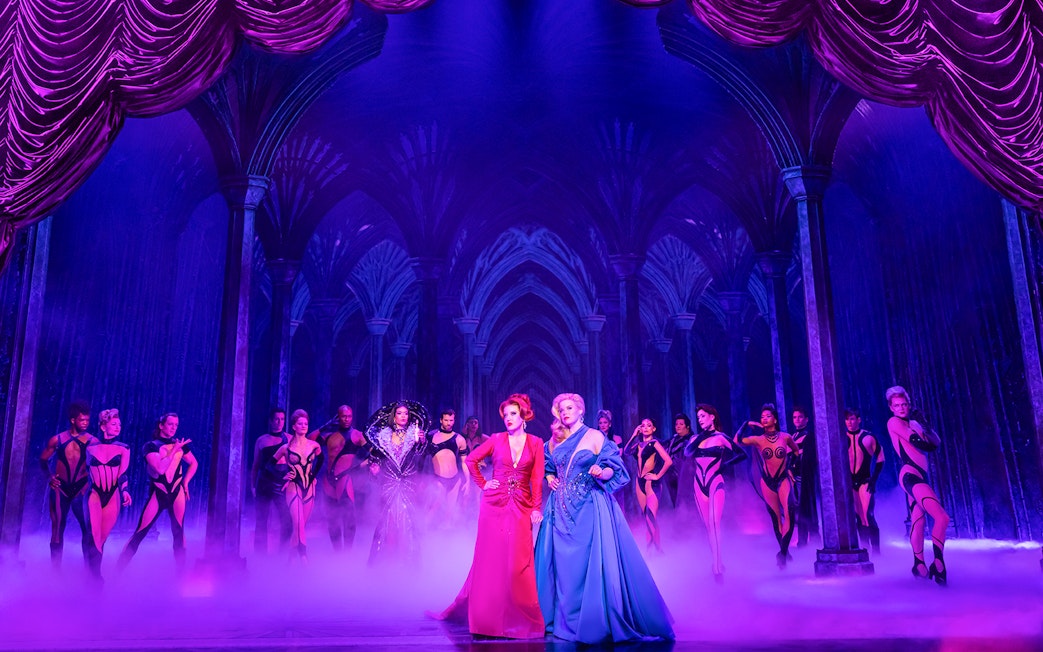 Theatrical performance of "Death Becomes Her" with actors in vibrant costumes on stage.