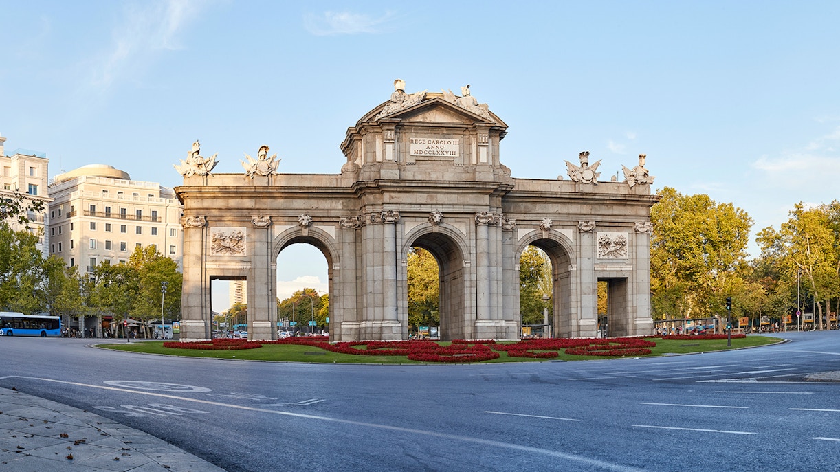 Puerta de Alcalá in Madrid surrounded by trees and cityscape.