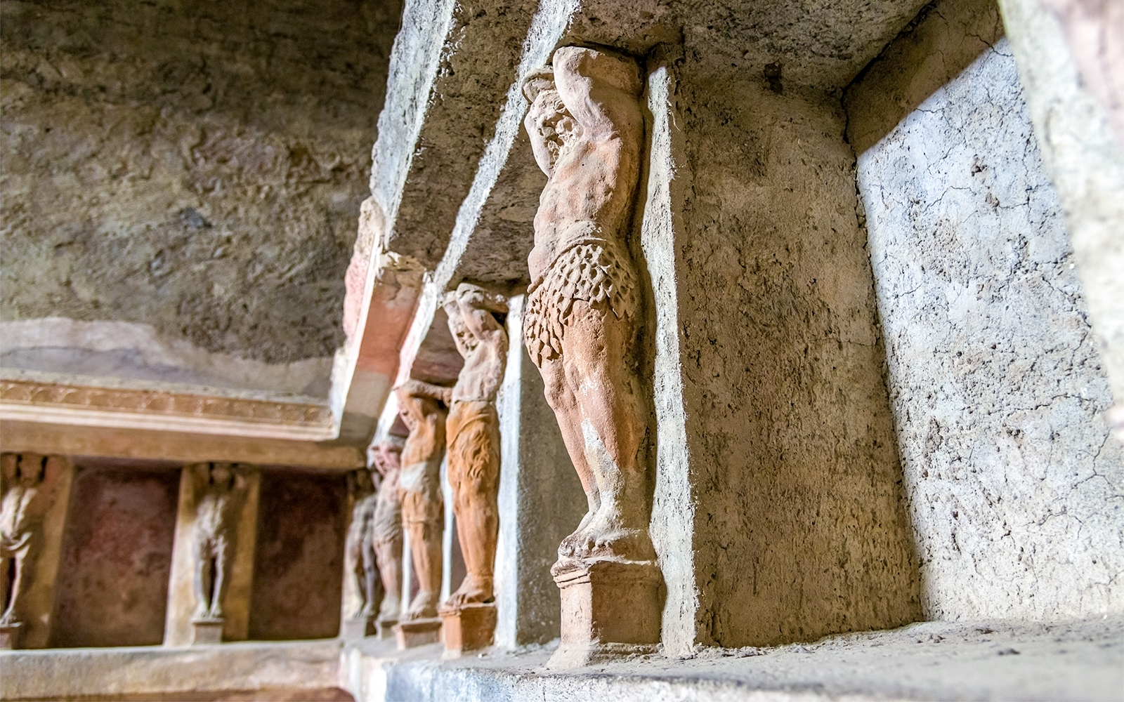 Ancient statues in the Pompeii Baths, Italy, depicting figures supporting a structure.