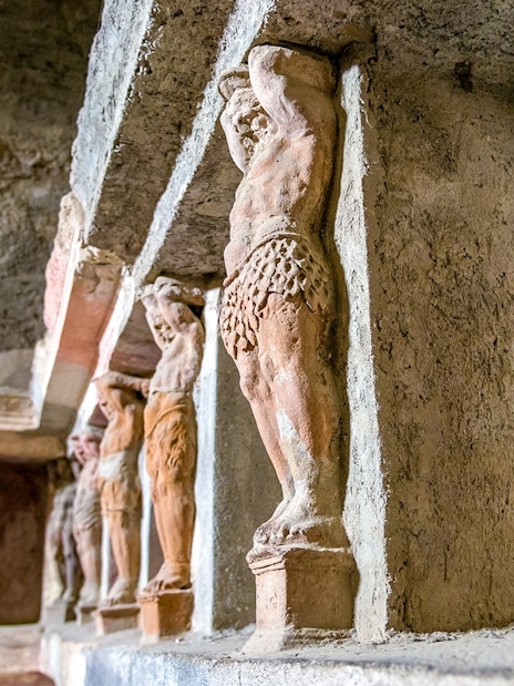 Ancient statues in the Pompeii Baths, Italy, depicting figures supporting a structure.