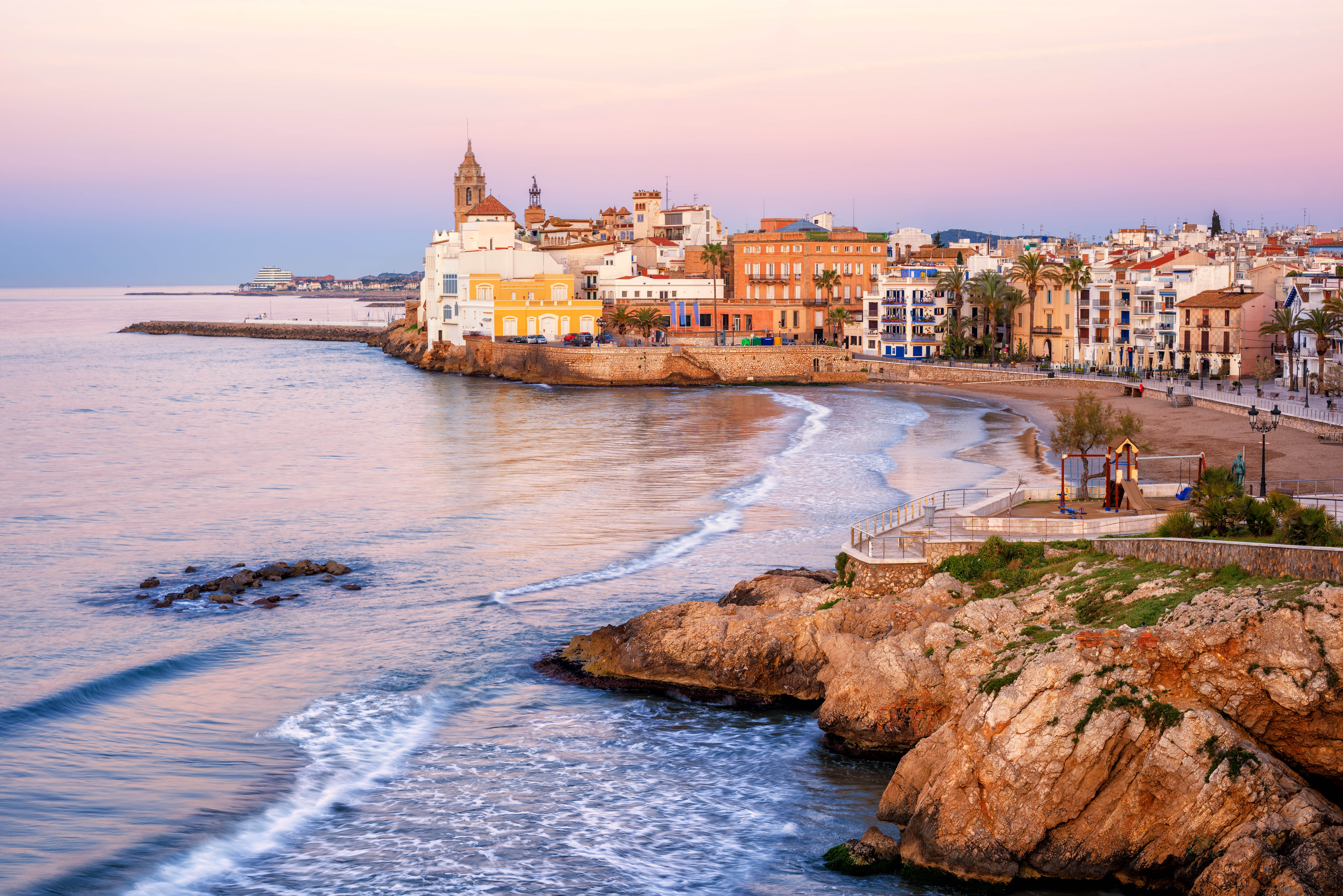 Sitges coastline at sunset with historic buildings and beach, part of Barcelona to Sitges tours.
