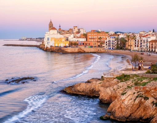 Sitges coastline at sunset with historic buildings and beach, part of Barcelona to Sitges tours.