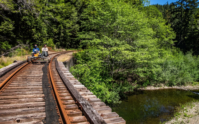 Guests riding rail bikes on Fort Bragg's Pudding Creek Express through lush forest scenery.