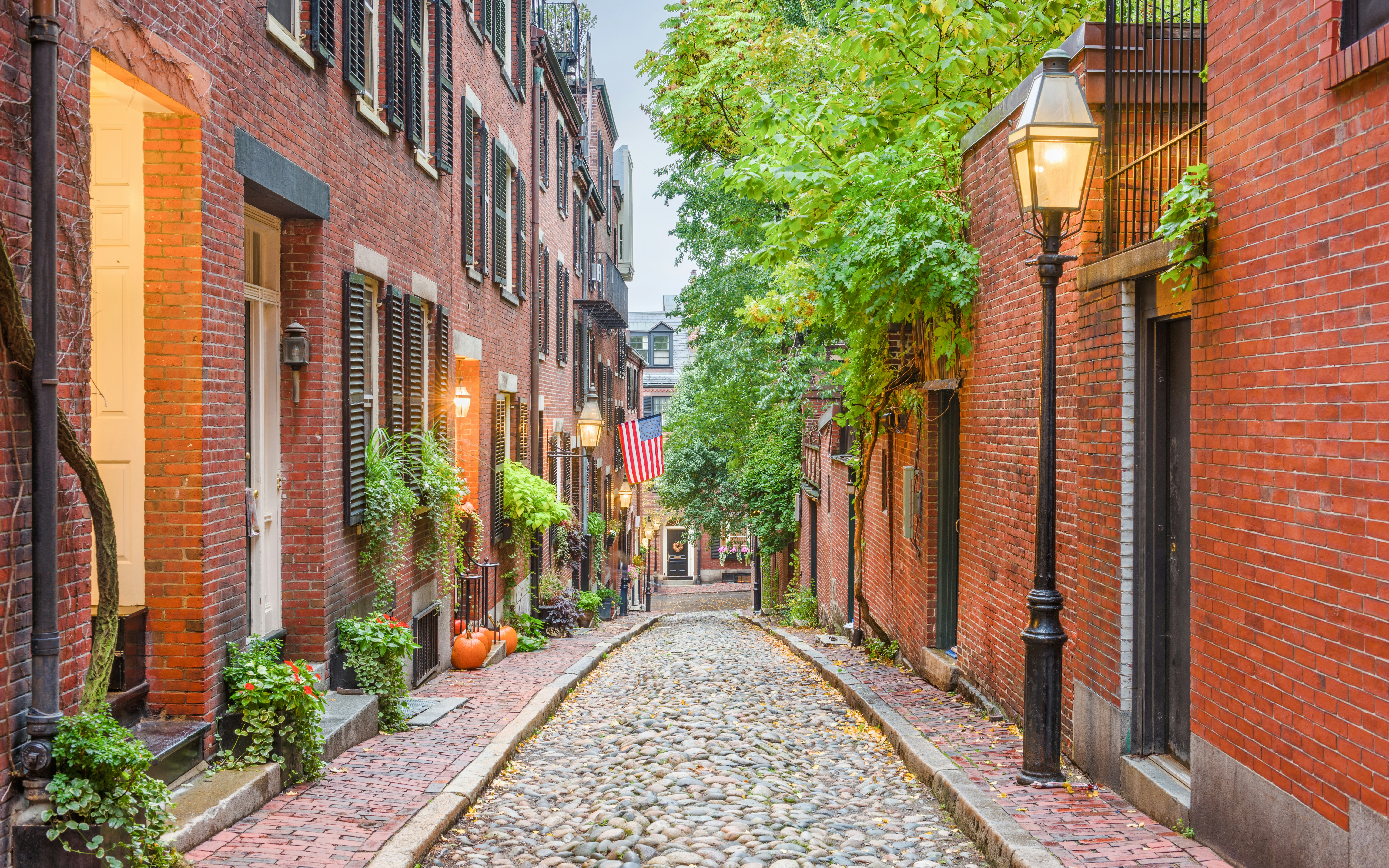 Cobblestone street in Beacon Hill, Boston with brick buildings and American flag.
