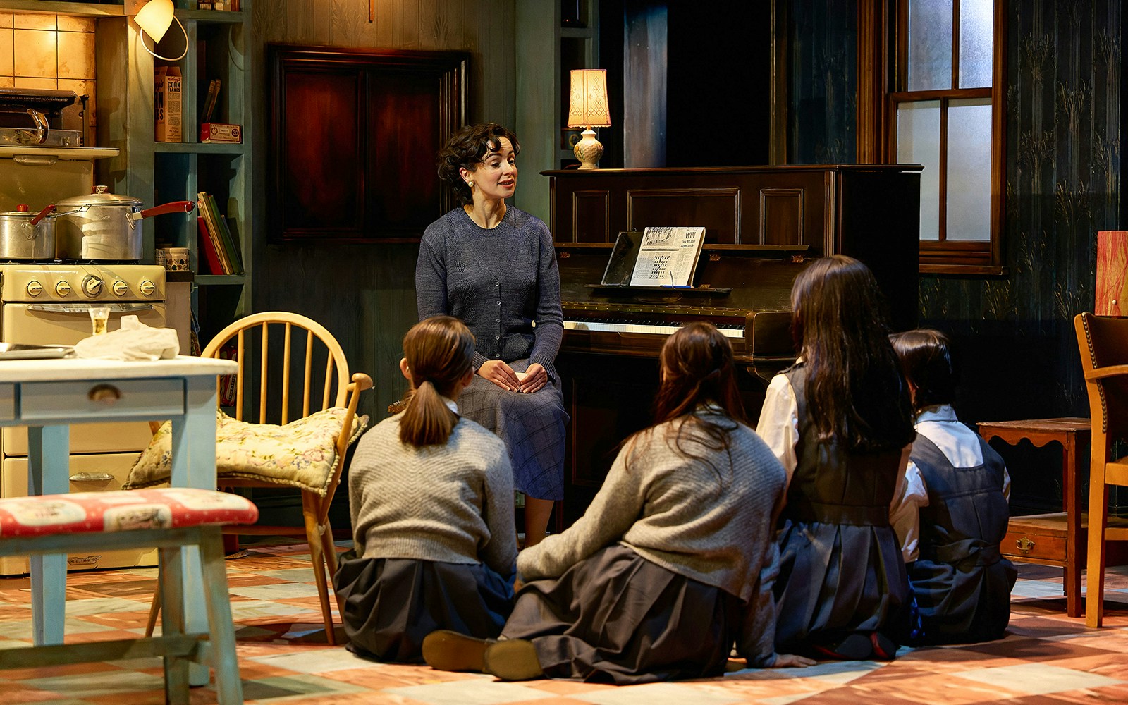 Woman speaking to children in a cozy room with a piano, set in The Hills of California.