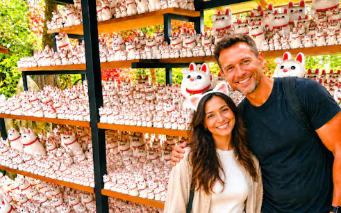 Visitors at Gotokuji Temple surrounded by shelves of lucky cat figurines, Tokyo.