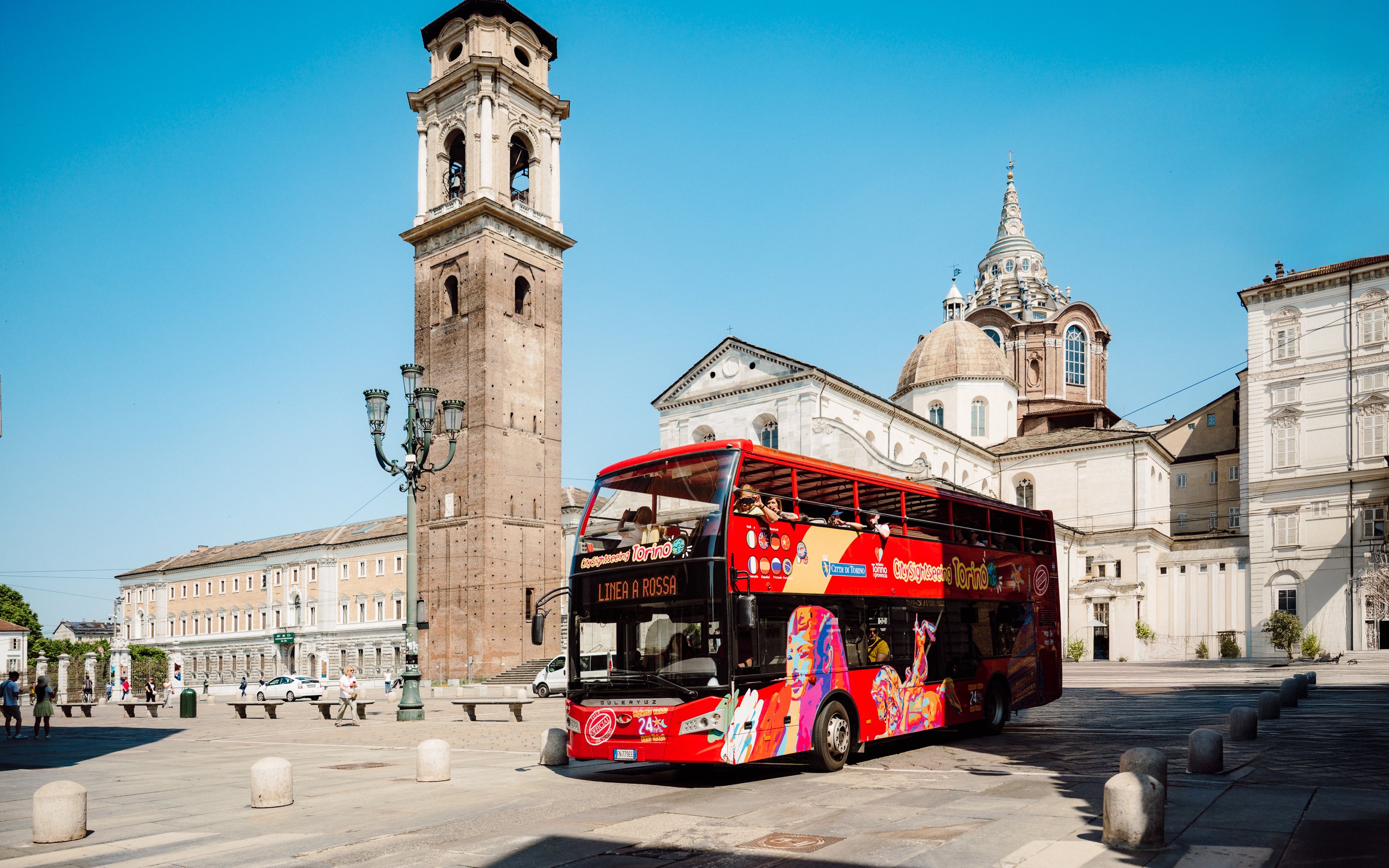 Hop-on hop-off bus near Turin Cathedral and bell tower in Turin, Italy.