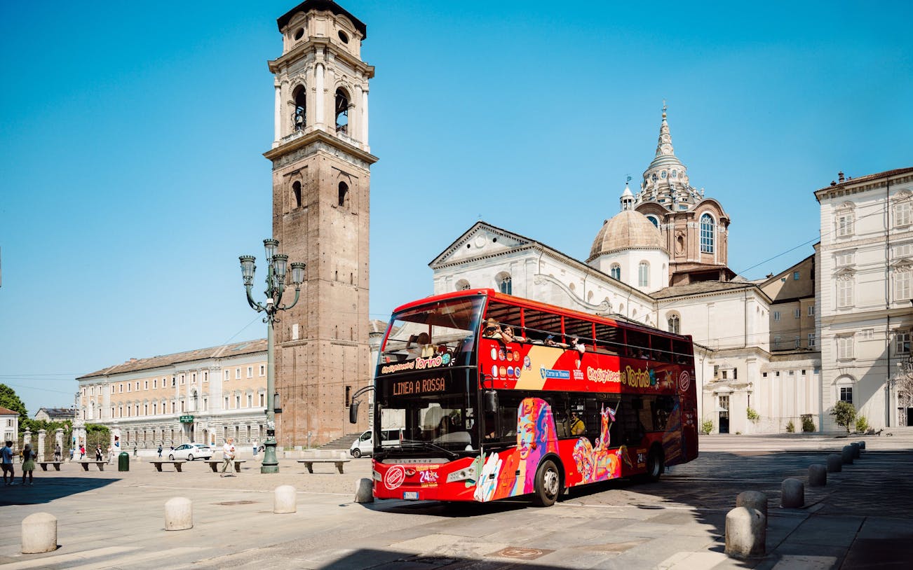 Hop-on hop-off bus near Turin Cathedral and bell tower in Turin, Italy.