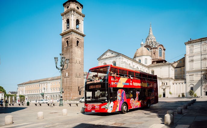 Hop-on hop-off bus near Turin Cathedral and bell tower in Turin, Italy.
