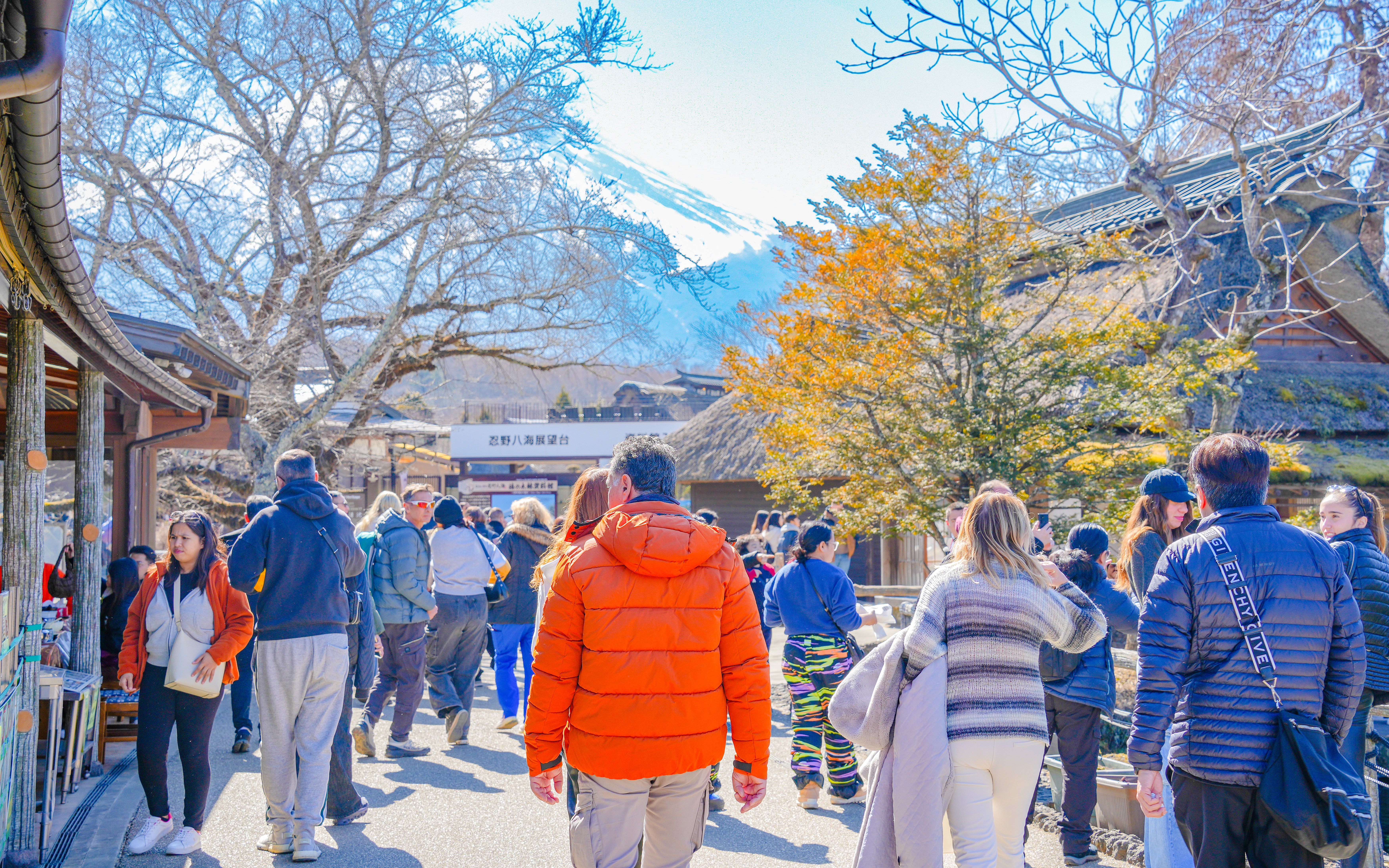 Tourists walking in a village near Mount Fuji with snow-capped peak in the background.