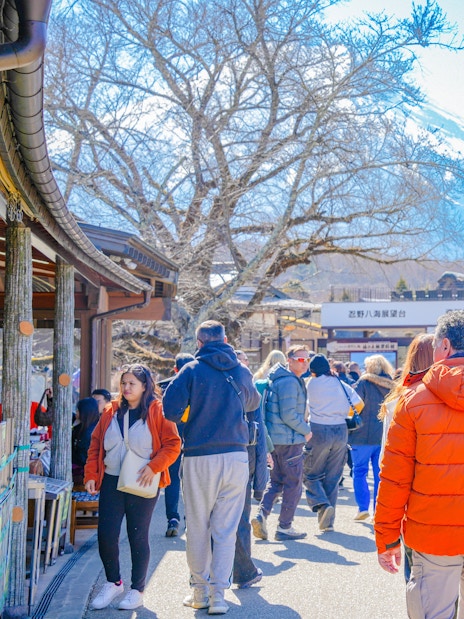Tourists walking in a village near Mount Fuji with snow-capped peak in the background.