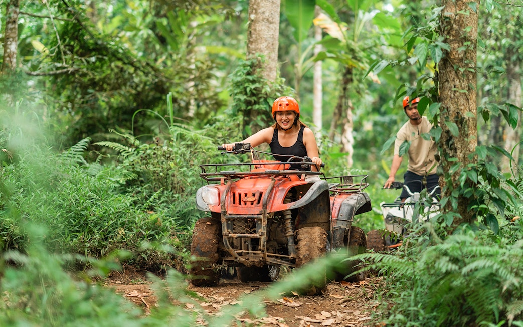 Asian couple riding ATVs through a forest track at an ATV arena.