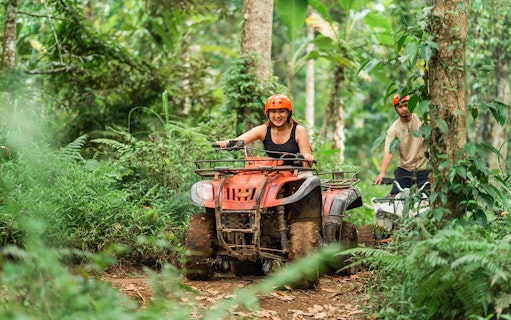 Asian couple riding ATVs through a forest track at an ATV arena.