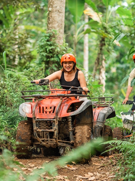 Asian couple riding ATVs through a forest track at an ATV arena.