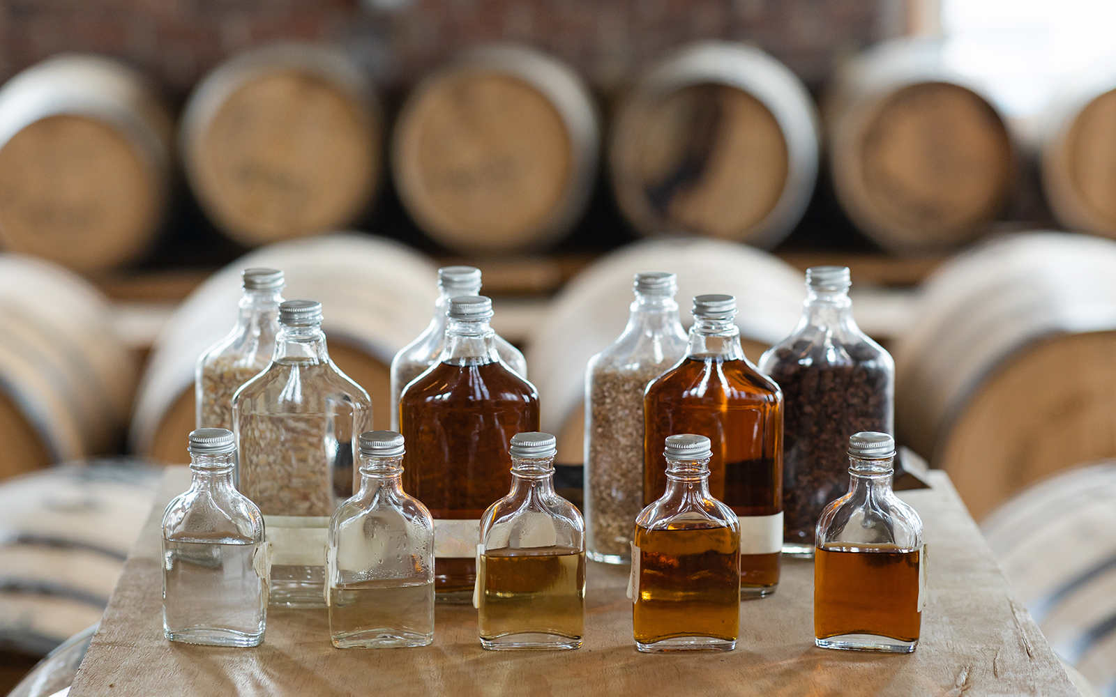 Whiskey tasting bottles with barrels in a distillery.