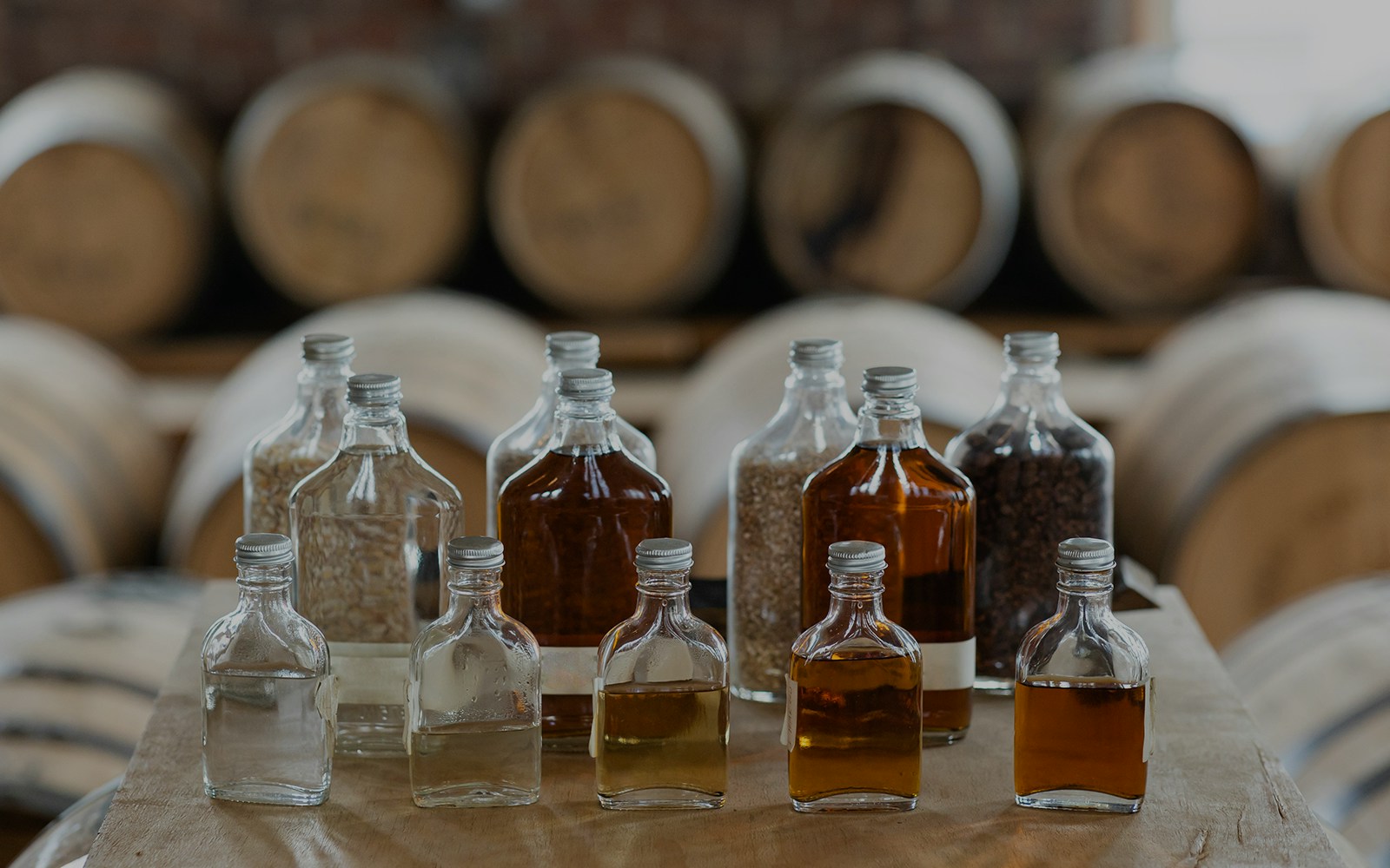 Whiskey tasting bottles with barrels in a distillery.