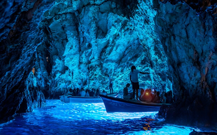 Boat tour inside Blue Cave on Bisevo Island, Croatia, with blue light illuminating the water.