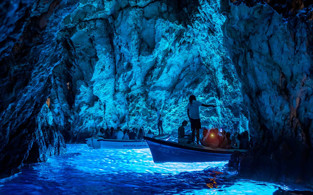 Boat tour inside Blue Cave on Bisevo Island, Croatia, with blue light illuminating the water.