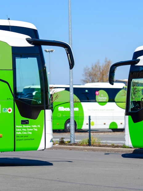Green airport shuttle buses parked in a lot, flibco.com branding visible.
