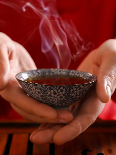 Master presenting steaming tea cup during traditional ceremony.