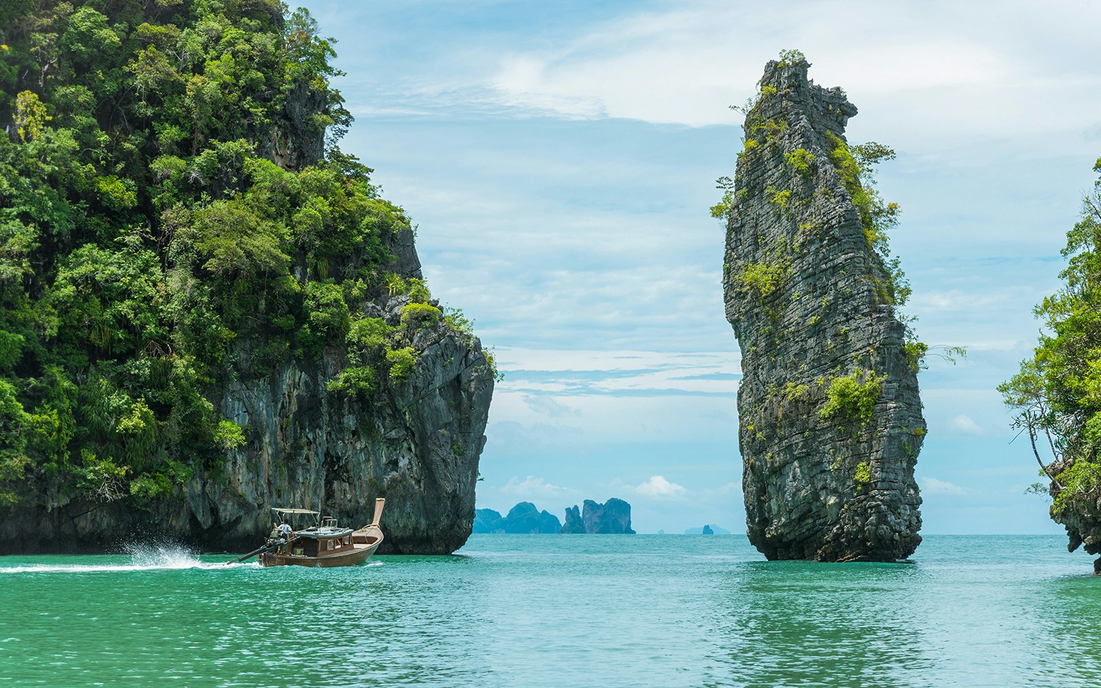 Longtail boat cruising between limestone cliffs in Phang Nga Bay, Thailand.