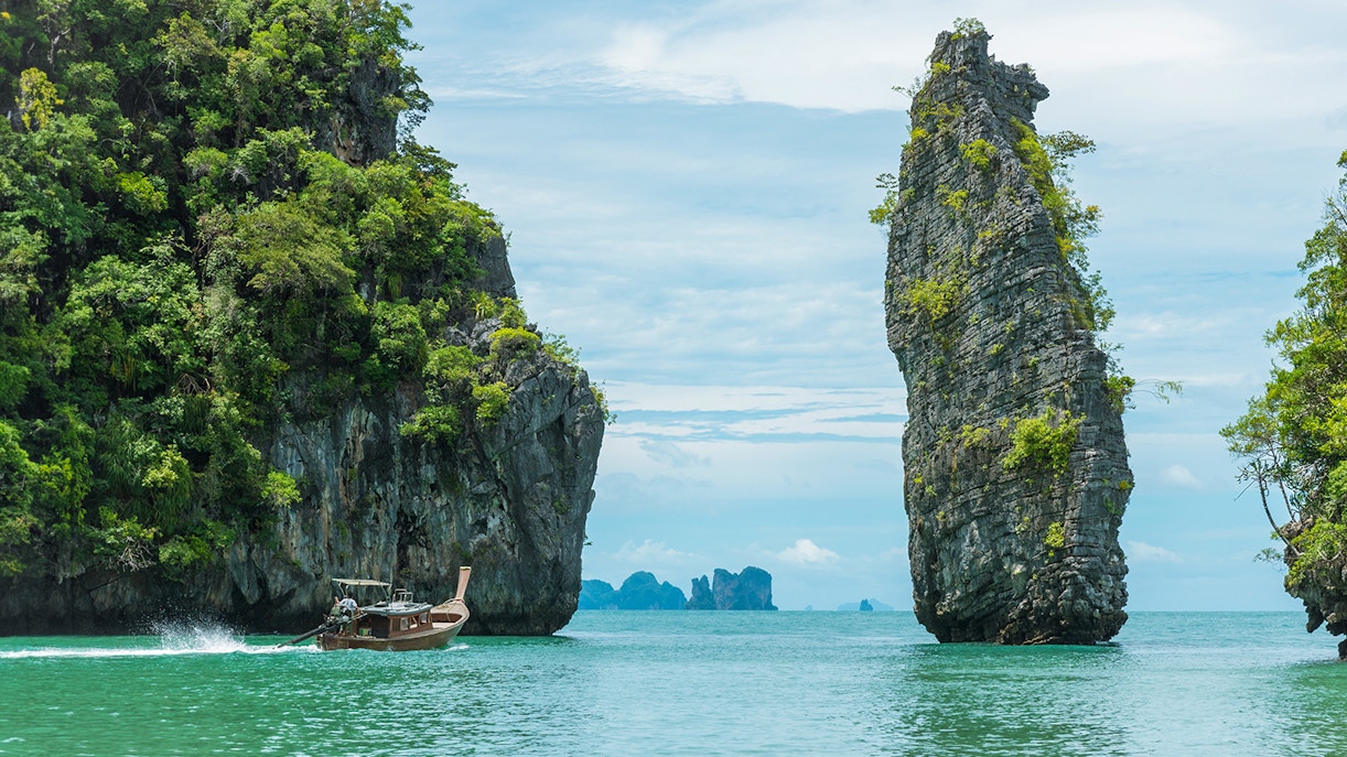 Longtail boat cruising between limestone cliffs in Phang Nga Bay, Thailand.