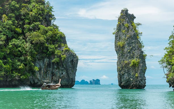 Longtail boat cruising between limestone cliffs in Phang Nga Bay, Thailand.