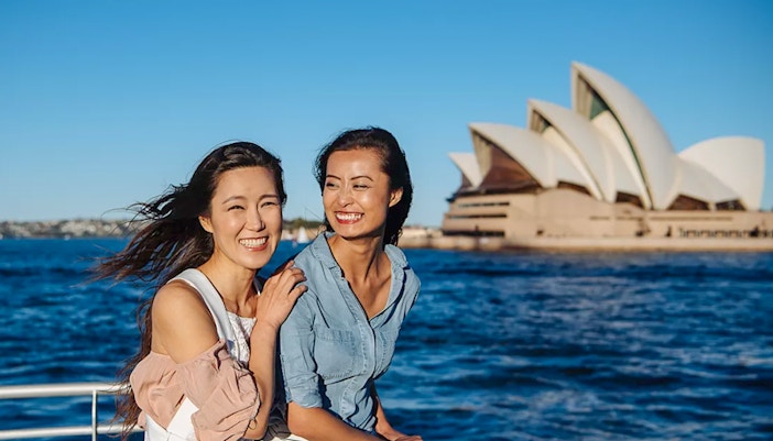 Women enjoying a whale watching cruise with Sydney Opera House in the background.