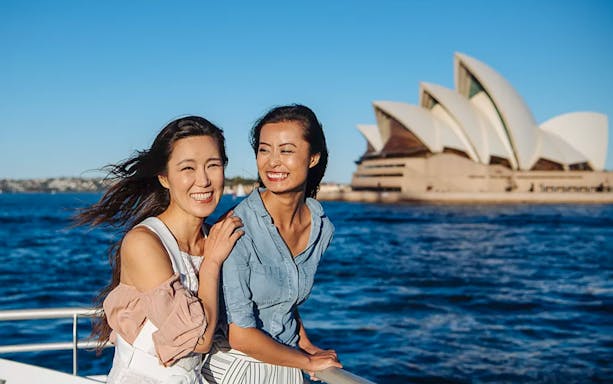 Women enjoying a whale watching cruise with Sydney Opera House in the background.