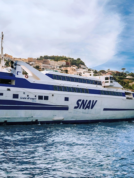 SNAV ferry approaching Capri with coastal town and cliffs in the background.