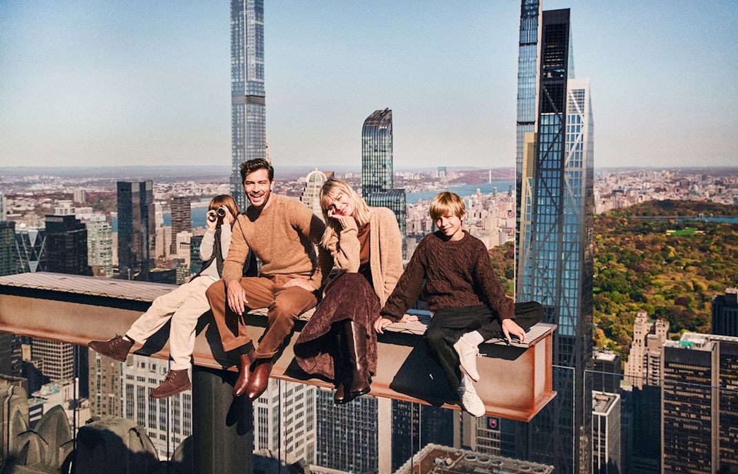 Guests sitting on a beam with New York City skyline view at Top of the Rock.