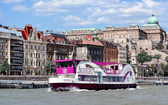 Cruise boat on the Danube River with Budapest architecture in the background.