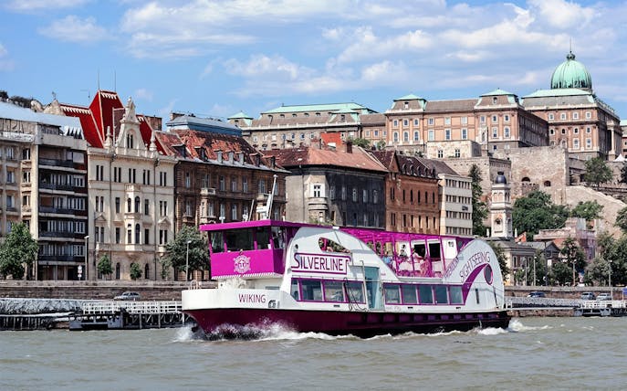 Cruise boat on the Danube River with Budapest architecture in the background.