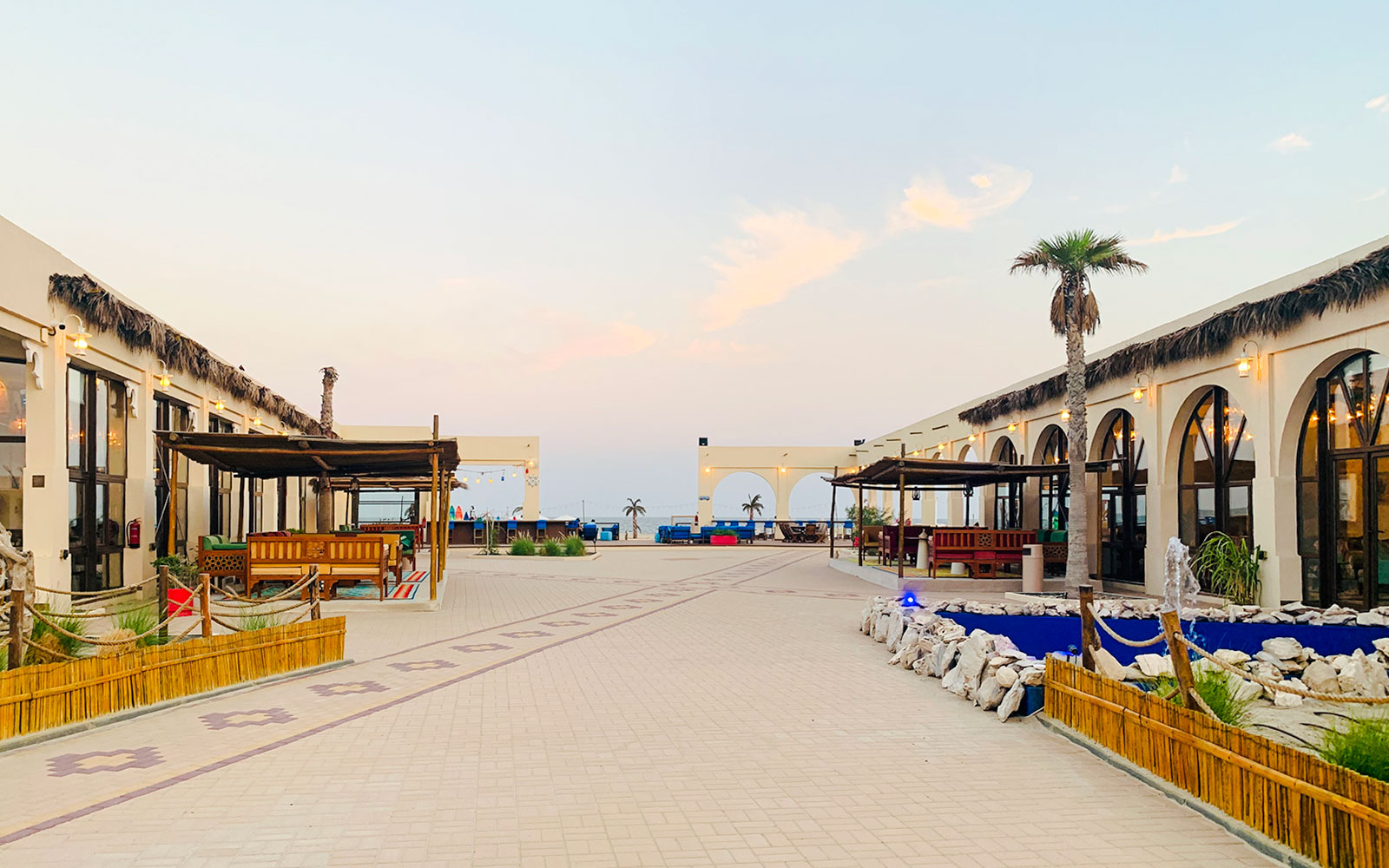 Al Majles Resort courtyard with palm trees and seating areas at sunset.