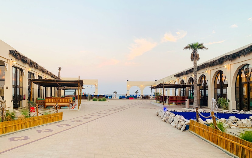Al Majles Resort courtyard with palm trees and seating areas at sunset.