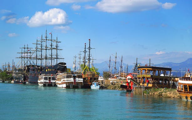 Boats docked along the Manavgat River, Turkey, with mountains in the background.
