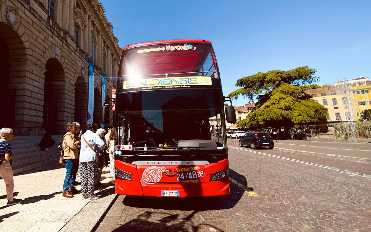Verona hop-on hop-off tour bus with passengers boarding near historic buildings.