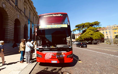 Verona hop-on hop-off tour bus with passengers boarding near historic buildings.