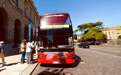 Verona hop-on hop-off tour bus with passengers boarding near historic buildings.