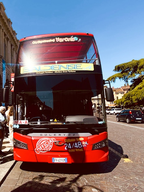 Verona hop-on hop-off tour bus with passengers boarding near historic buildings.