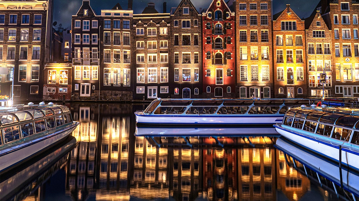 Canal boats in front of illuminated Amsterdam buildings during the Light Festival.