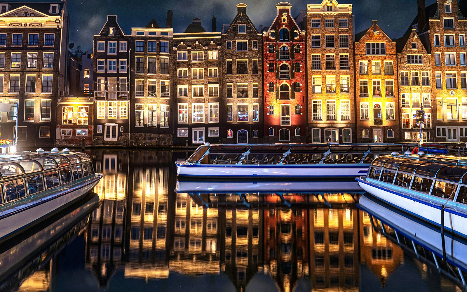 Canal boats in front of illuminated Amsterdam buildings during the Light Festival.