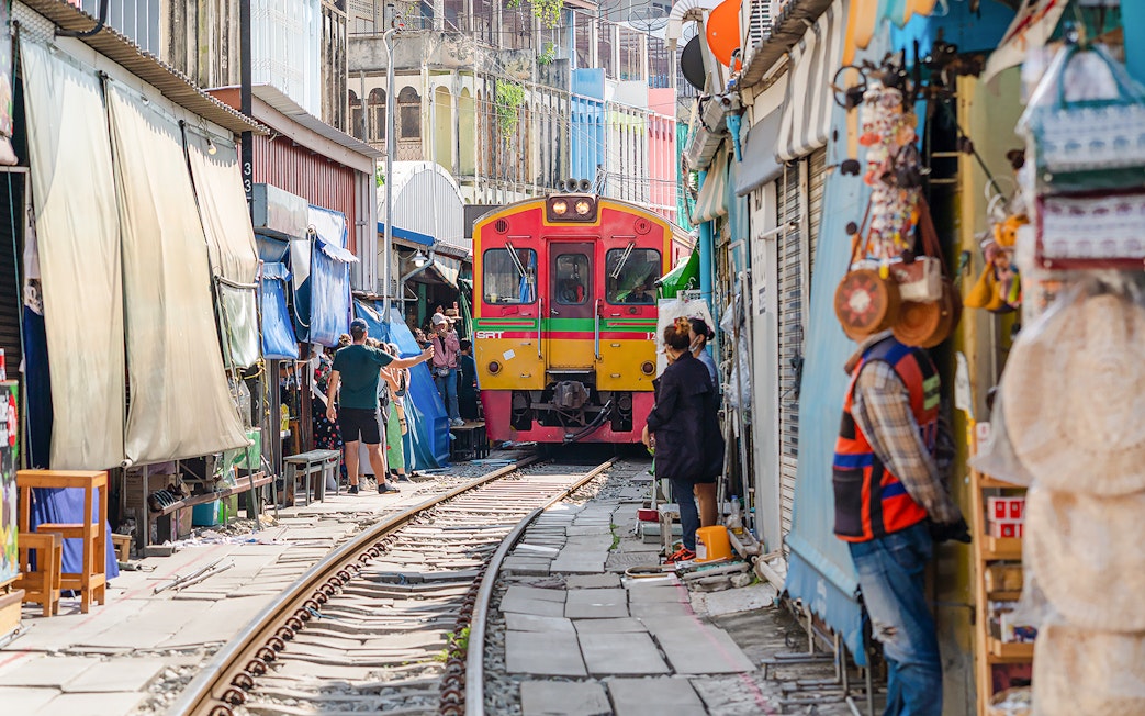 Train passing through Maeklong Railway Market with tourists and vendors nearby.